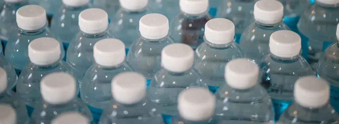 macro shot of rows of clear plastic water bottles with white caps; plastics greenwashing is bad