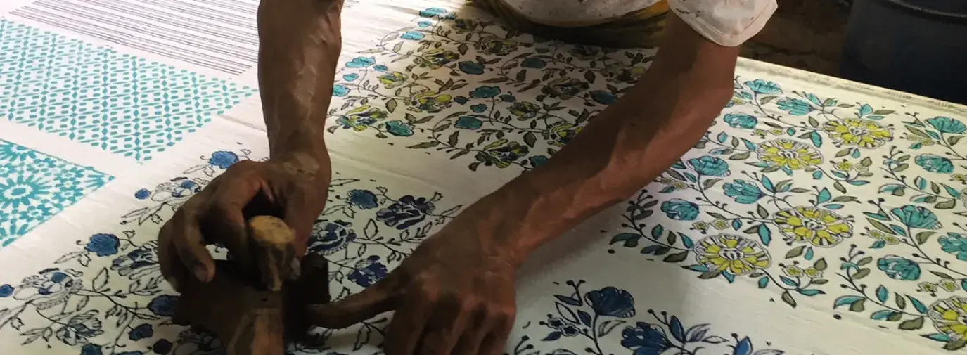 Indian man bends over a piece of cloth and applies a floral wood block print. Title: More than the Minimum: Why We Need a Livable Wage