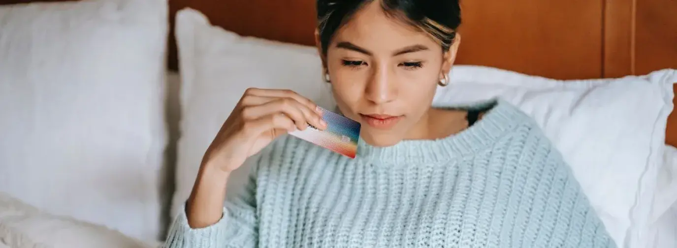 woman in a blue sweater holding her credit card while she shops online