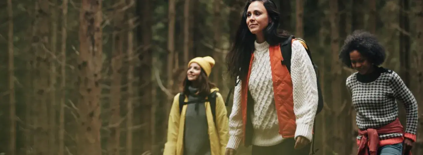 three women hiking in sweaters in a lush green forest