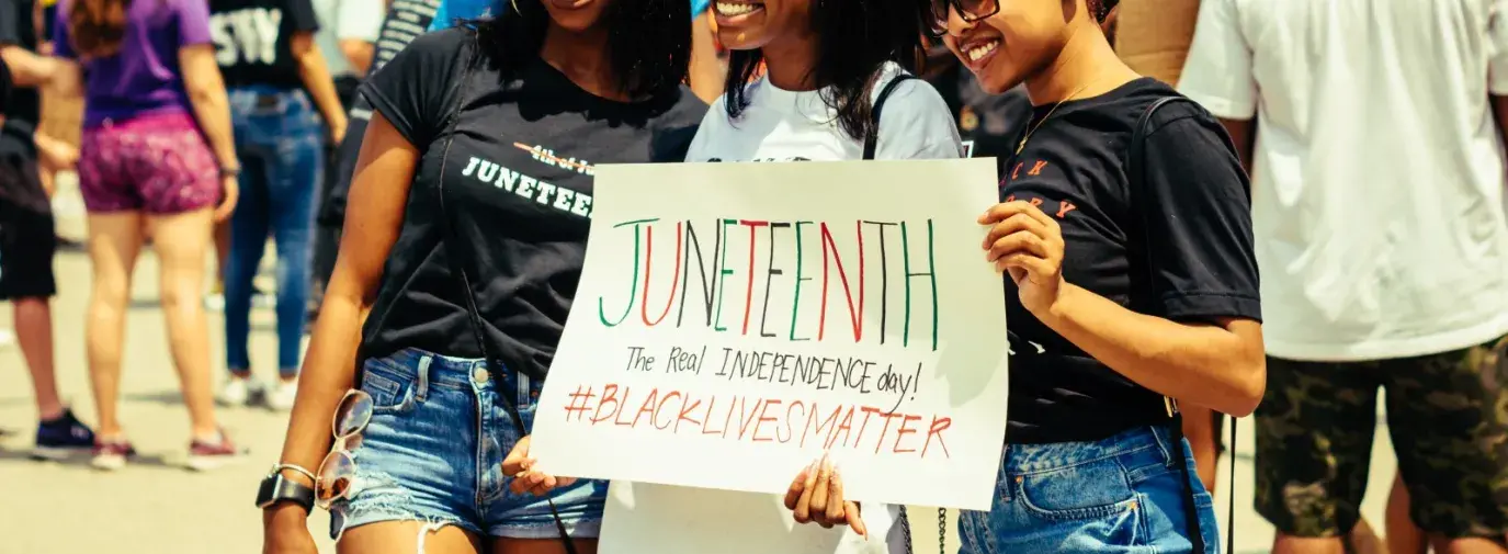 Three young Black women hold a sign that says Juneteenth at a public event