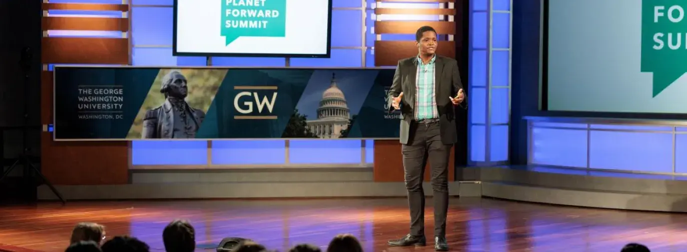 Matt Scott in a black suit giving a presentation to an audience at George Washington University's 2022 Planet Forward Summit