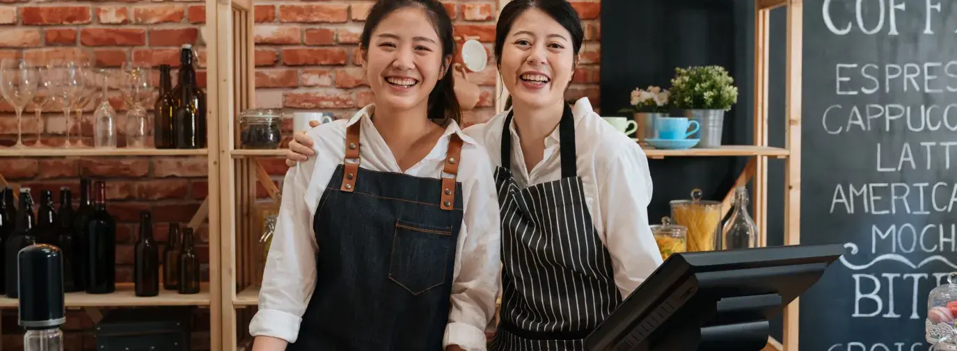 mother and daughter wearing aprons and smiling. They are coffee shop owners ready to make coffee.