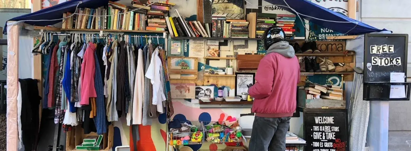 a person in a red jacket and black pants browsing the shelves of a Free Store in Green Point.