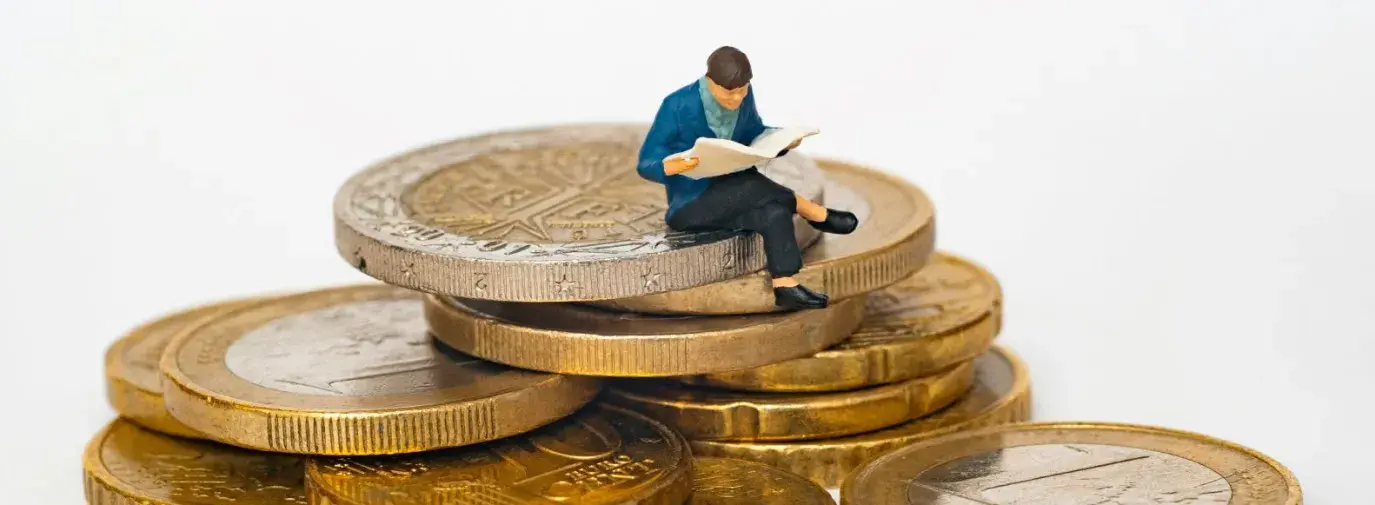 miniature figure of a person in a blue jacket sitting on top of a stack of gold coins.