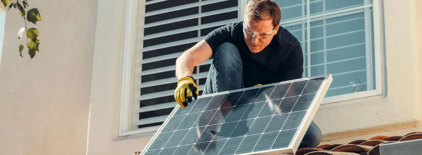 A man on a roof placing a solar panel. 