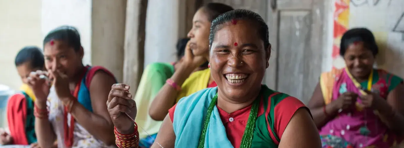Nepali women dressed in colorful traditional attire making beaded bracelets. 