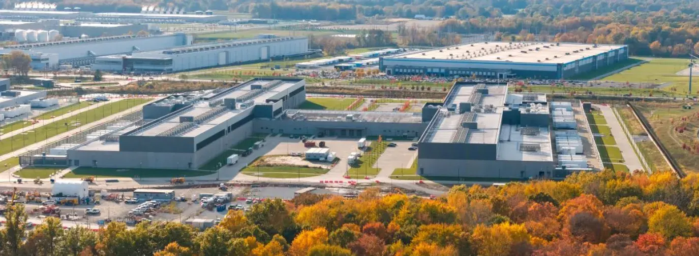 wide shot of a data center in Ohio from a hillside, so you can see the entire metropolis of warehouses. In the foreground are orange and yellow trees in the fall.