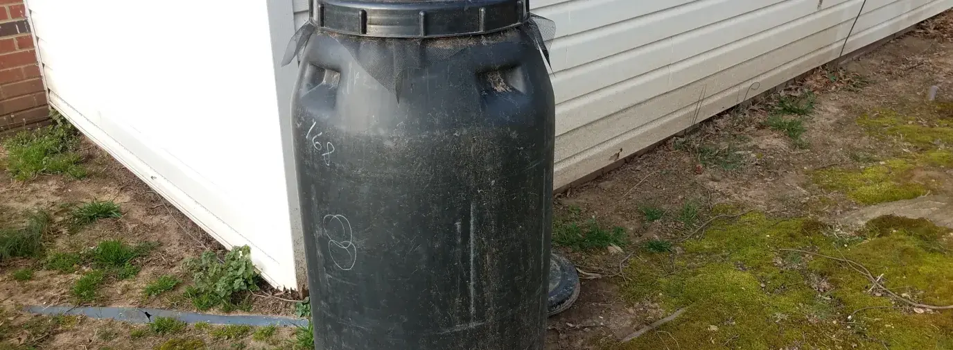 black rain barrel next to white house, build your own rain barrel for your climate victory garden