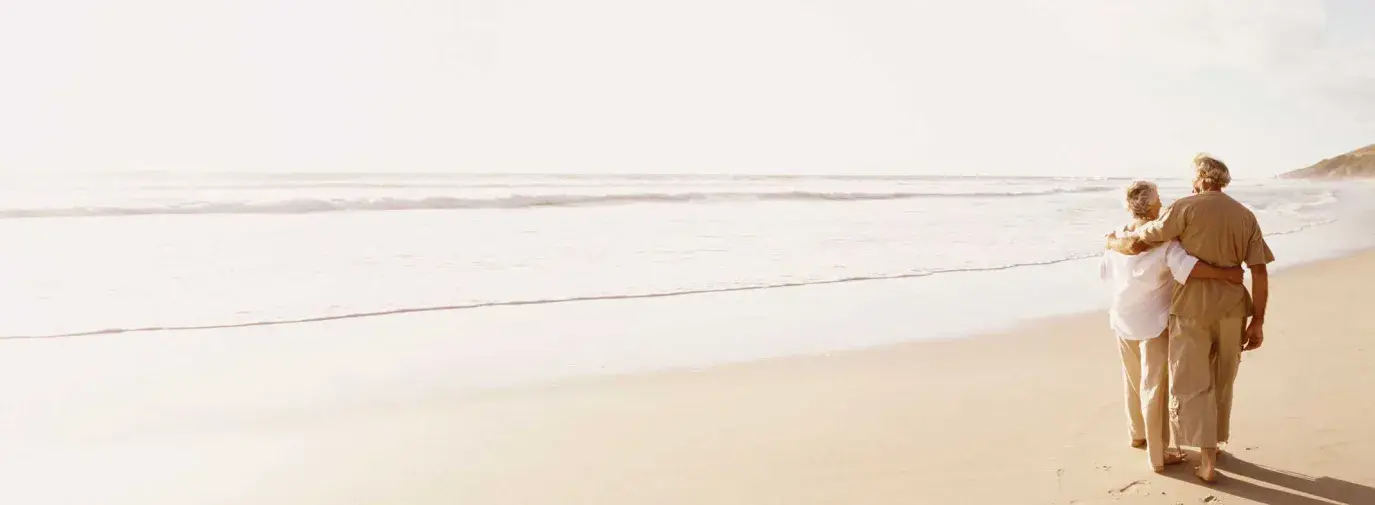 A retired couple walking arm-in-arm down the beach, people who can be helped by Sustainable Wealth Advisors