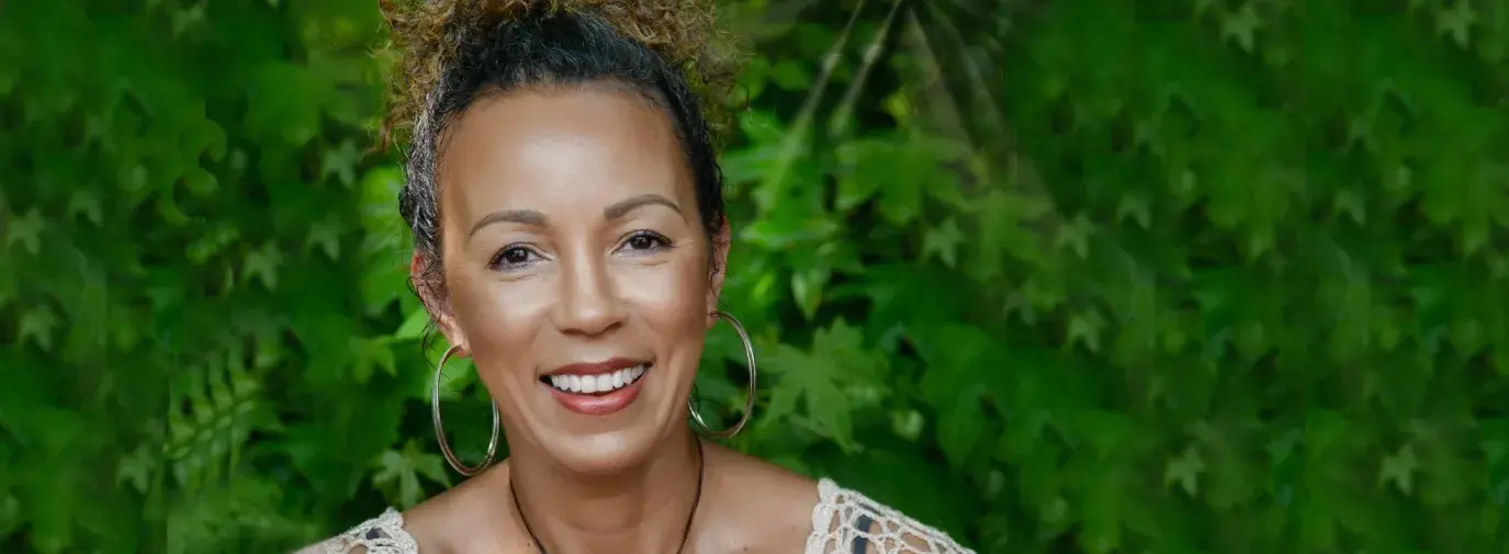 Founder and CEO of SMB Essentials, Lake Louise, smiles at the camera. She is wearing a crocheted beige top, large hoop earrings, and a handmade circle necklace. 