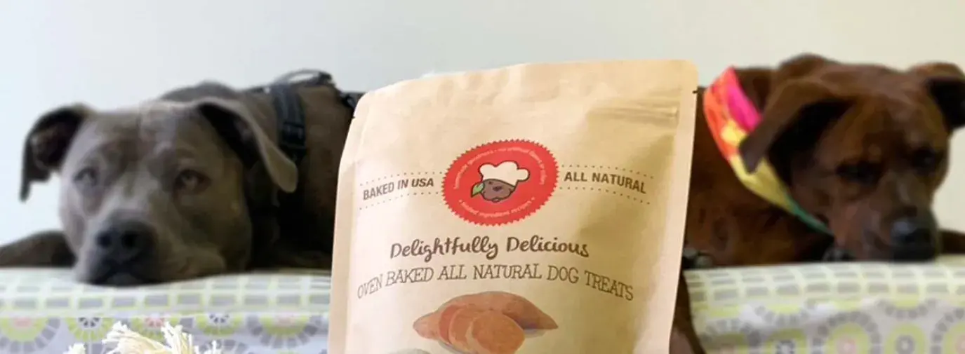 bag of dog toys from what's good in front of two dogs lying on a dog bed