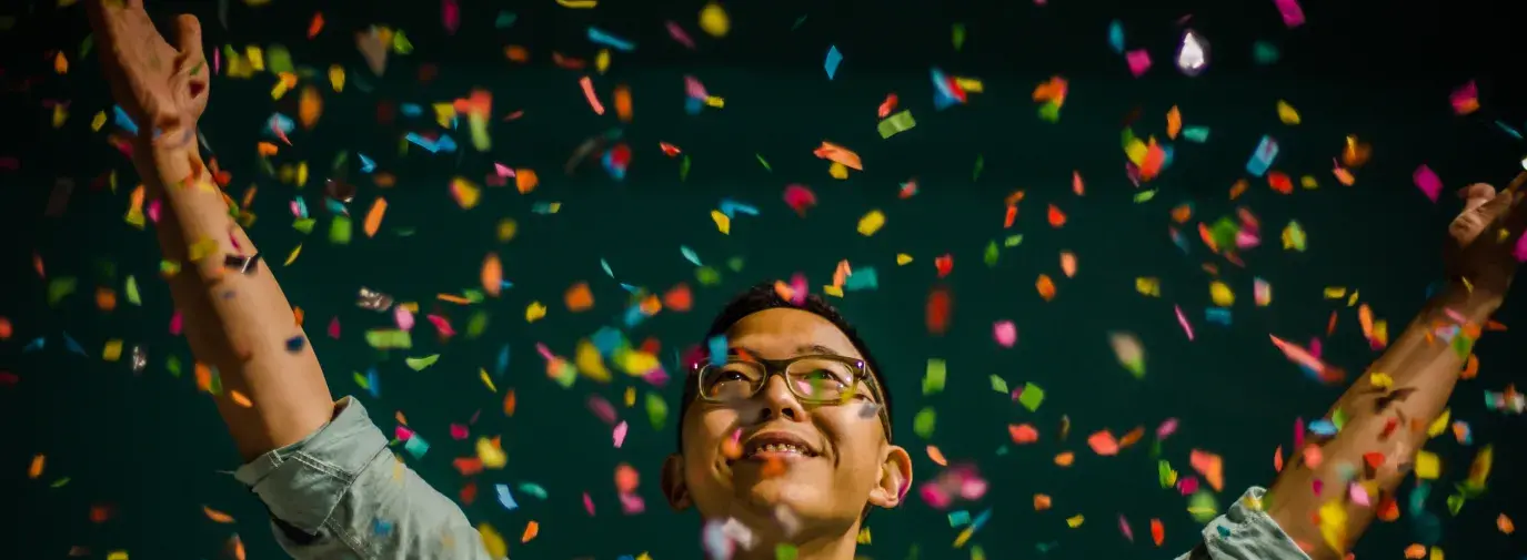 Person celebrating with multi-colored confetti. Topic: Green America’s Guide to Sustainable Gifts, Holidays, and Special Occasions.