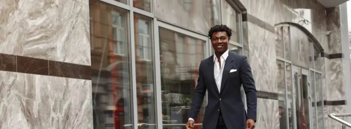 black man in suit walking with paper bags in hand. 
