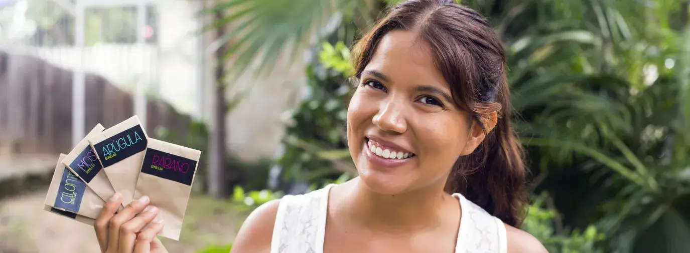 Smiling woman holding paper seed packets in a garden