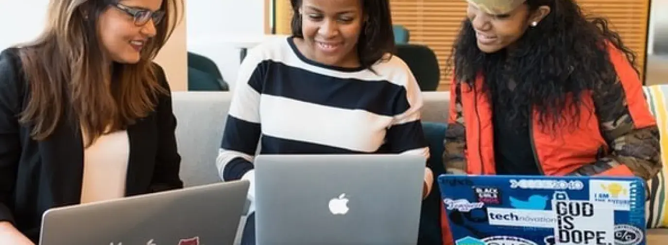 three women sit together with laptops 
