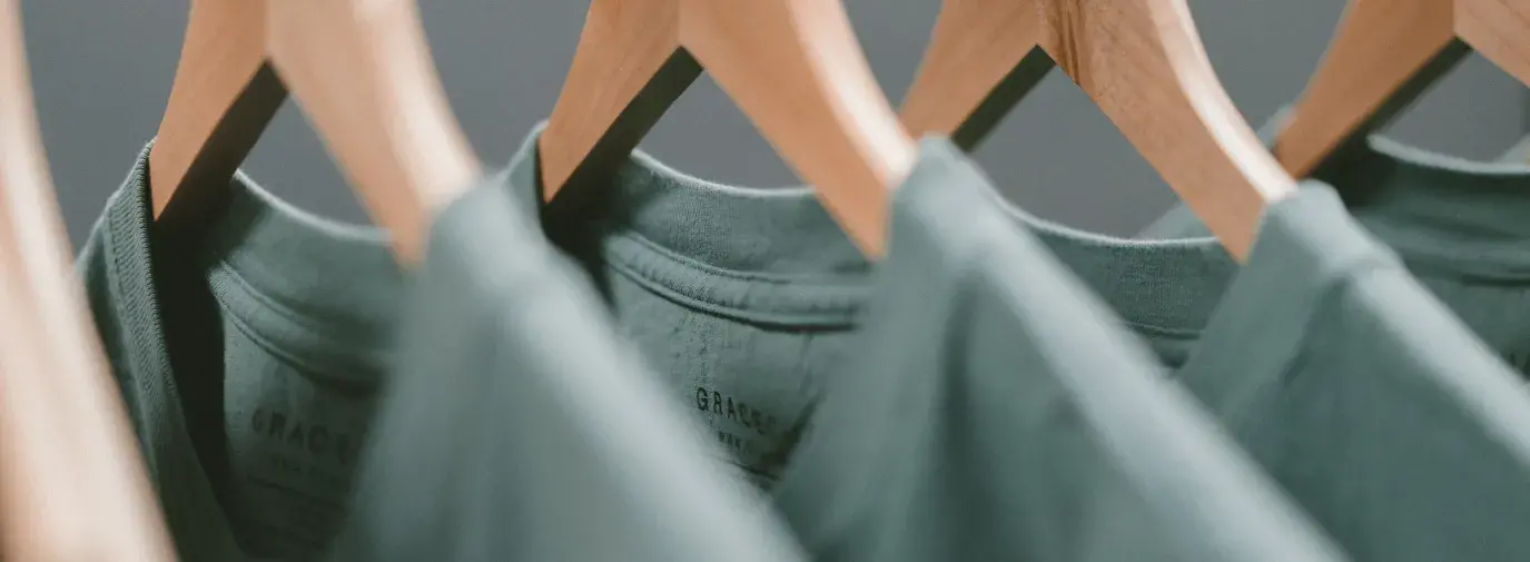 three green t-shirts on wooden hangers
