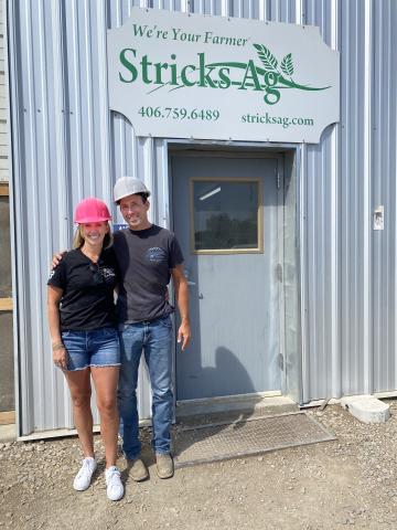 Jill and Tyler Streit wearing hard hats and posing happily outside the Stricks Ag processing facility. 