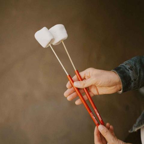 A pair of hands holding marshmallows on reusable skewers. Sustainable summer.