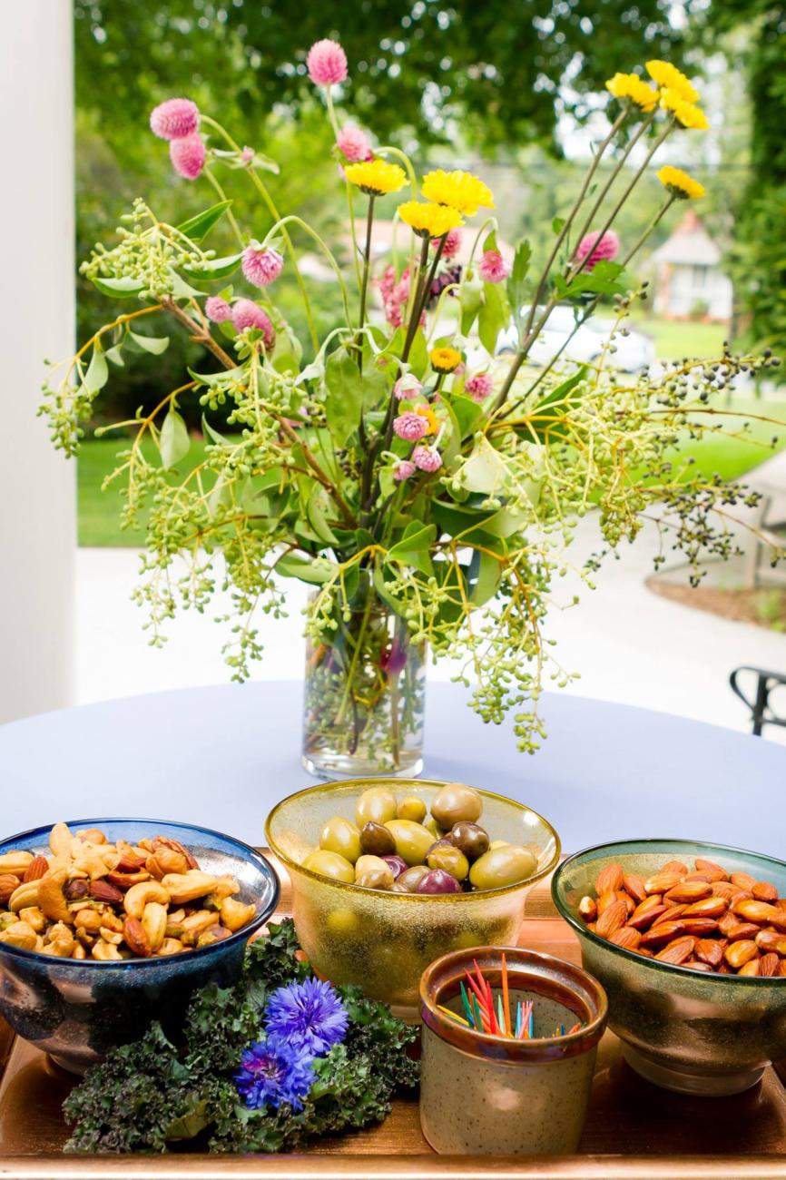 A spread of olives and nuts with a vase full of wildflowers behind it