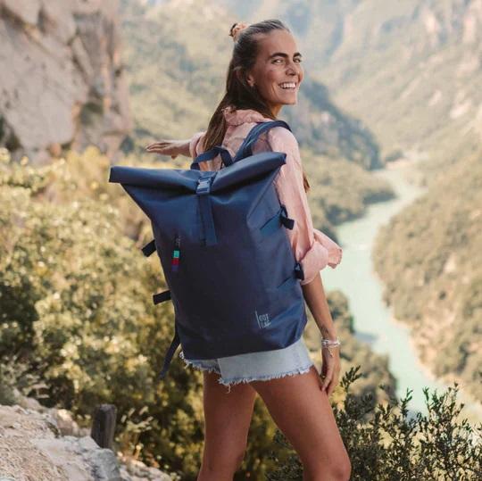 Woman wearing a recycled rolltop backpack and looking over her shoulder. Sustainable summer.