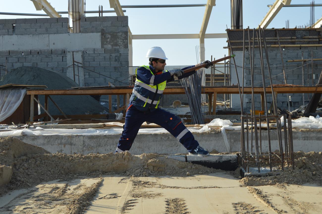A construction worker wearing a white hard had and reflective yellow vests works on a construction site, standing in sand. Inflation Reduction Act.