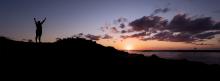 Image: person standing victorious on hilltop overlooking ocean and sunset: Topic: Green America's victories.