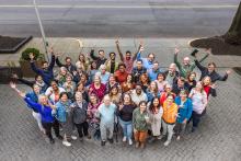 the Green America staff and Board grouped together smiling at the camera. Everyone is doing the ASL sign for I love you. 