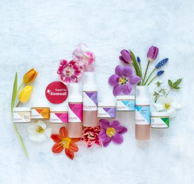 A line of colorful skincare products in bottles surrounded by colorful flowers
