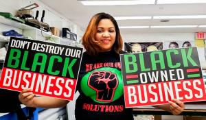 Keeanna Barber of WDB Marketing holds signs that say "Don't destroy our Black Business" and "Black Owned Business" that she printed at her shop.
