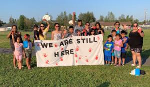 Indigenous activists holding a sign that reads "we are still here"