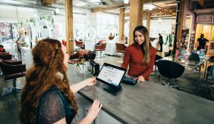 A small, industrial style store, a redheaded white woman checks out an Asian woman at the counter; the IRA has several new small business resources