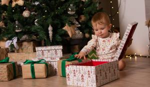 A baby opening Christmas presents in front of a decorated tree. The presents are in boxes and brown paper. Fair Trade Gift Guide.