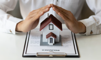 Hands over a miniature house sitting on an insurance policy